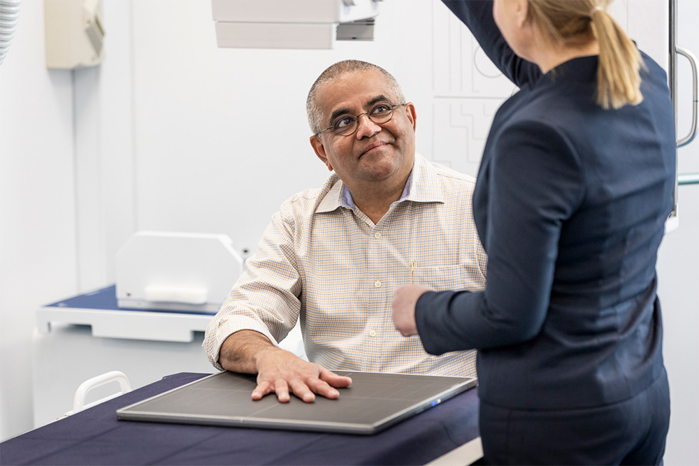 Man with hand spread and placed with female radiographer preparing him for a hand x-ray