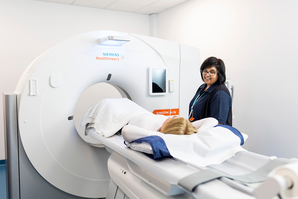 Radiographer discussing CT scan with patient lying on bed of CT.
