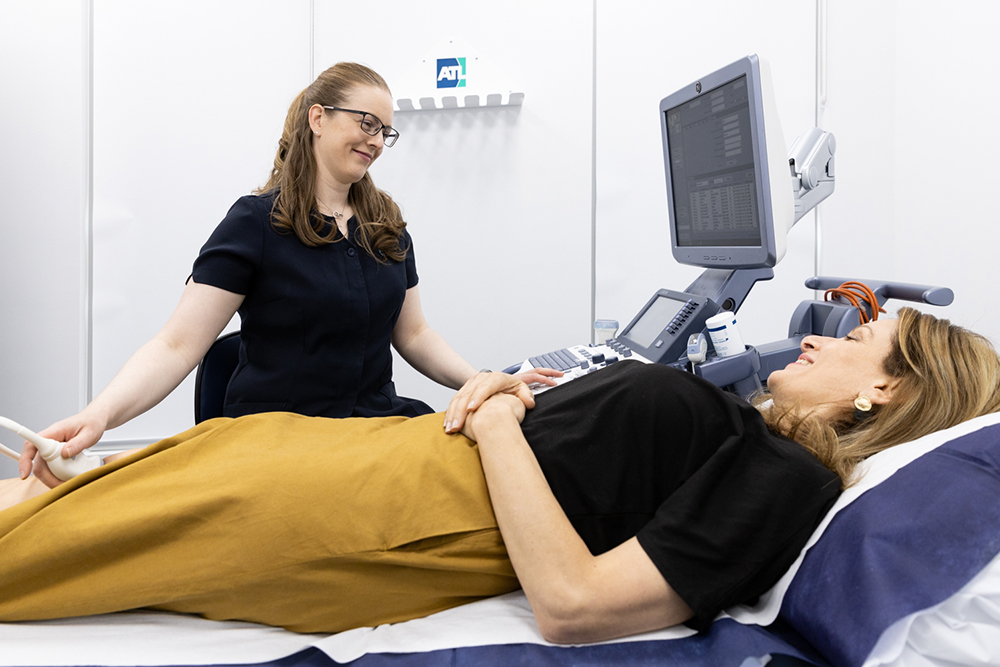 Female patient lying on bed while a female sonographer performs ultrasound on her knee