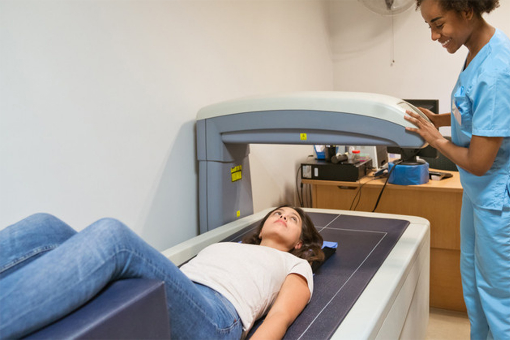 Young woman lying on a bone densitometry machine with a female radiographer explaining the process of the scan